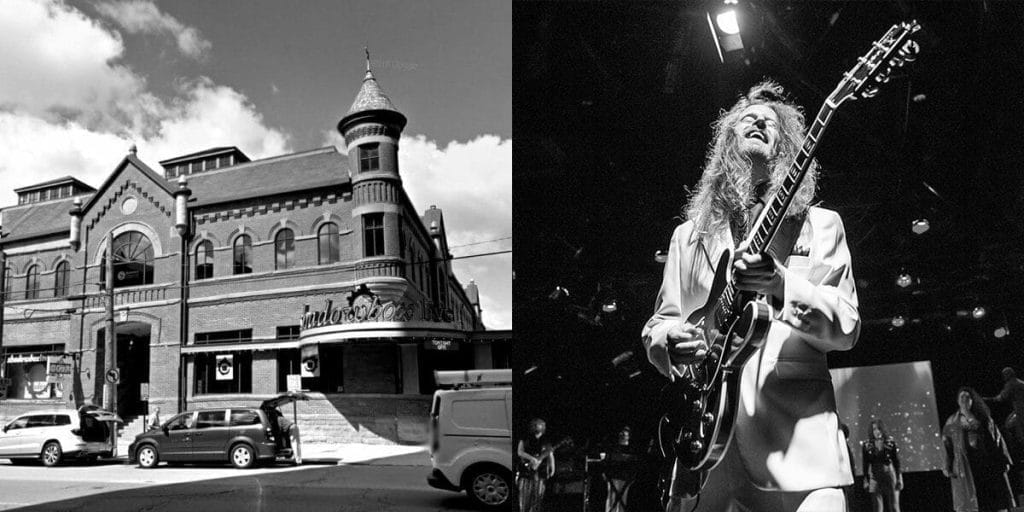 A black and white photo of a man playing a guitar in front of a building.