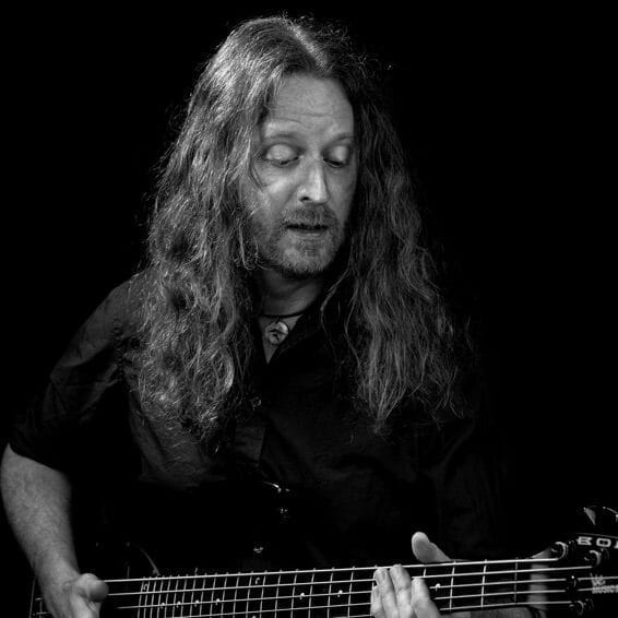 A man with long hair playing a bass at an education event.