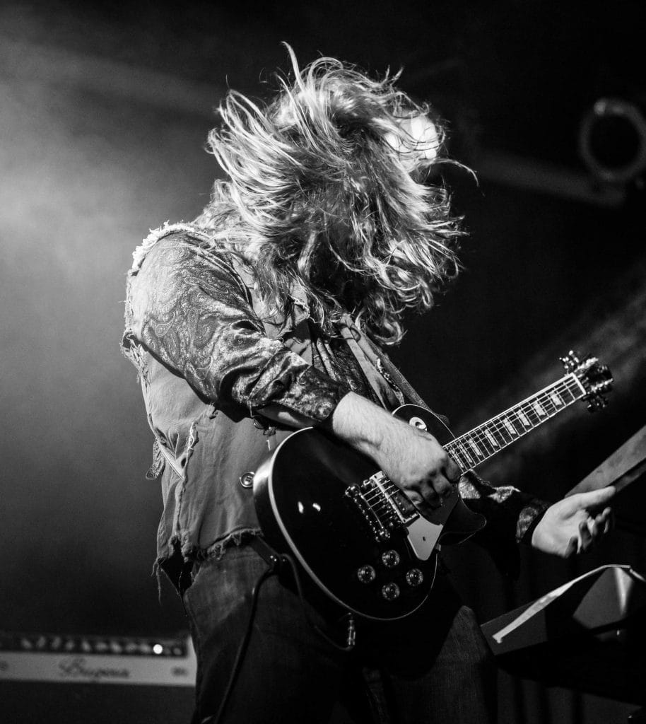 A man with long hair playing a guitar on stage.