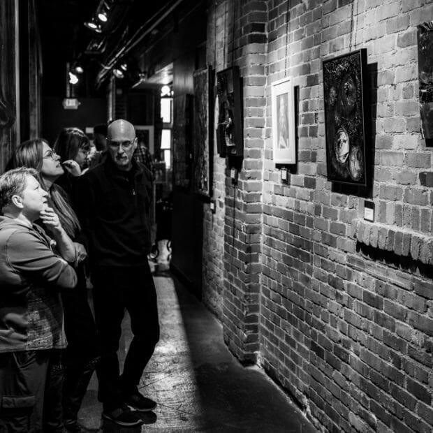A black and white photo of people looking at art in an alley.